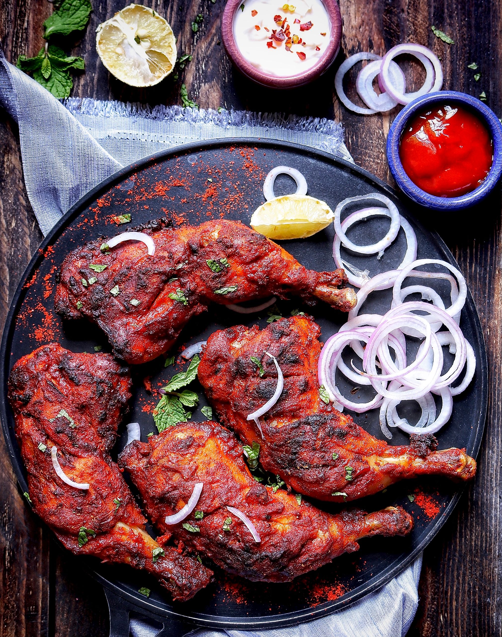 Delicious grilled chicken with onion rings and spicy sauces on a rustic platter.